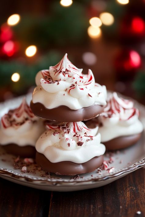 Chocolate-dipped meringue cookies topped with crushed candy canes on a plate, with holiday lights and ornaments in the background. Peppermint Meringues Recipe, Merengue Cookies Peppermint, Flavored Meringue Recipe, Meringue Christmas Cookies, Peppermint Meringue Cookies, Meringue Cookie, Marange Cookies, Christmas Meringue Cookies, Chocolate Chip Meringue Cookies