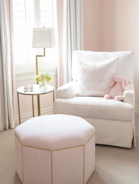 A beautiful white nursery glider topped with a white and pink pillow is paired with a pink stripe octagon ottoman paired with a round marble and brass accent table and lit by a brass floor lamp. Dainty Nursery, Transitional Nursery, Pink And Green Nursery, Pink Painted Walls, Striped Nursery, Pink And Gray Nursery, Girl Nursery Pink, White Crib, Chic Nursery