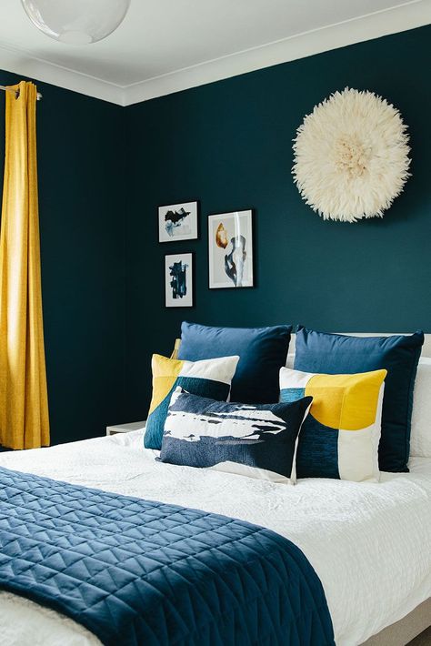 We love using dark blues to warm up a space. The pops of sunshine yellow in this bedroom scheme also add a welcome contrast and bring some energy back to the space - perfect for those mornings in the Autumn and Winter time where you might need a bit of encouragement out of bed! This room is so beautifully decorated that it could be a 5-star hotel room! Click the link to see how you can make your master bedroom so beautiful that you'll never want to leave! 🛏️ Guest Bedroom Ideas Black, Bedroom Blue And Gold, Bedroom Ideas Black And White, Ochre Bedroom, Dark Blue Bedroom Walls, Blue Yellow Bedrooms, Dark Blue Rooms, Bedroom Ideas Black, Teal Rooms