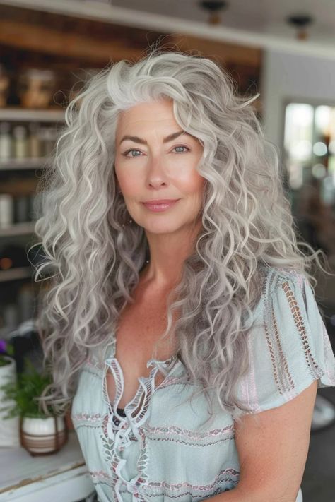 Woman with long, curly gray hair and a serene expression, wearing a light-colored blouse. Long Curly Hair For Older Women, Grey Hair Ideas Going Gray, Long Gray Shag Hairstyles, Curly Gray Hairstyles, Ash Blonde Curly Hair, Curly Grey Hair, Long Gray Hair Over 50, Curly Haircuts For Women, Curly Silver Hair