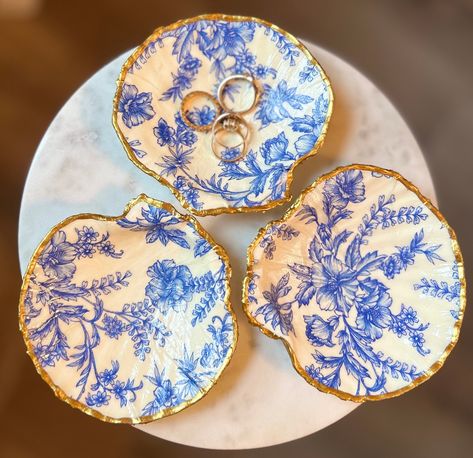 Elegant blue floral handmade individual scalloped seashell trinket dish. Can be used for rings or other jewelry. The perfect summer/bridal gift!  Each of my decoupage shells is a one-of-a-kind creation, carefully crafted with love and care. Due to the natural variations in the shells and the handmade nature of the decoupage process, no two shells are exactly alike. Shell size and shape can vary. This means the shell you receive will be uniquely yours, with its own individual charm and character.   Materials used: decorative paper, scalloped shells, gold enamel, decoupage medium Back of the shell is the natural shell with gold enamel trim.  All shells are triple coated to ensure quality will last. Decoupage Shells, Decoupage Jewelry, Shell Ring Dish, Random Products, 15 Birthday, Perfect Engagement Gifts, Bed Side Table, Products Photography, Nails Colors