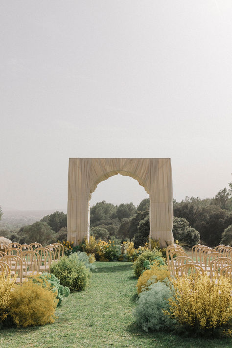 A serene ceremony setup in nature 🌿 This minimalist, elegant archway surrounded by lush greenery and soft yellow blooms creates the perfect backdrop for a romantic outdoor wedding. With simple wooden chairs and an open-air ambiance, it’s an idyllic spot to say 'I do.' 🌞 #OutdoorWedding #WeddingArch #NatureInspired #MinimalistWedding #CeremonyDecor Tree Backdrop Wedding Ceremony, Wood Aisle Wedding, Different Wedding Arch Ideas, Backdrop Ceremony Wedding, Simple Ceremony Backdrop Outdoor, Wedding Ceremony Arch Alternatives, Wedding Arch With No Flowers, Square Ceremony Arch, Wedding Ceremony Isles