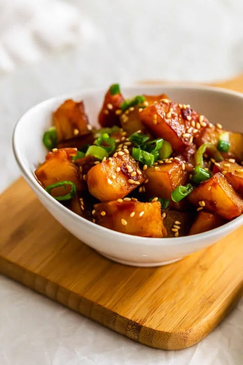 Close up of Korean potatoes in a white bowl on a wooden board. Korean Spicy Potatoes, Korean Braised Potatoes Recipe, Korean Banchan Potato, Korean Fried Potatoes, Korean Mashed Potatoes, Korean Style Potatoes, Japanese White Sweet Potato Recipes, Korean Bonchon Recipe, Asian Potatoes Side Dishes