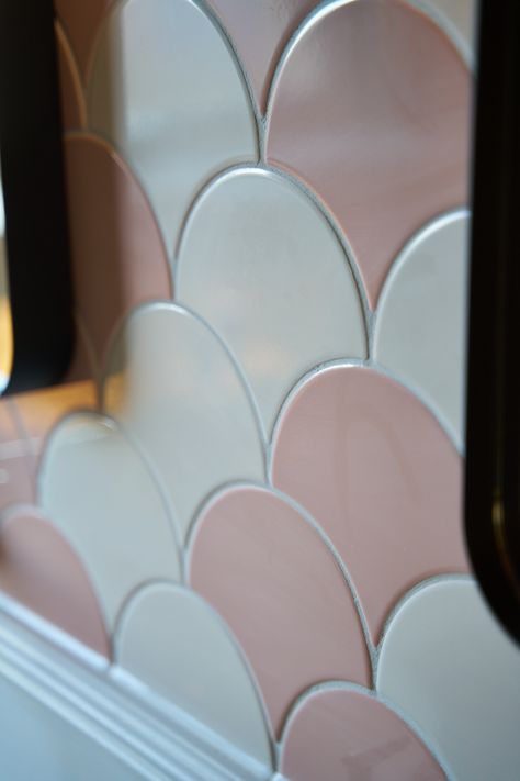 A close-up view of scalloped tiles in shades of soft pink and white, arranged in an overlapping pattern. The glossy finish of the tiles reflects light, adding a subtle shine to the surface. The delicate, curved shapes of the tiles create a soft, elegant look, ideal for adding a touch of charm to a bathroom or kitchen backsplash. The grout lines define each tile, enhancing the contrast between the pale pink and white hues. Pink Bathroom Design, Green And Pink Bathroom, Green Bathroom Design, Elegant Backsplash, Scallop Tiles, Pink Bathrooms Designs, Black Taps, Freestanding Bath, Unique Bathroom