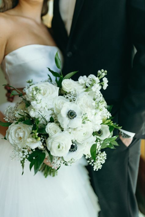 Close up photo of Bride holding a Bouquet filled with ivory roses, white anemone, ranunculus, babys breath, delphiniums and italian ruscus Bride Flower Bouquet White Anemones, White Roses And Anemones, Anemone Flower Bouquet Ranunculus, Black And White Anemone Bouquet, Bridal Bouquet White Peonies Ranunculus, Italian Ruscus Wedding Bouquet, White Bouquet With Anemones, Bridal Bouquet Classic Elegant, Bridal Bouquet With Anemones