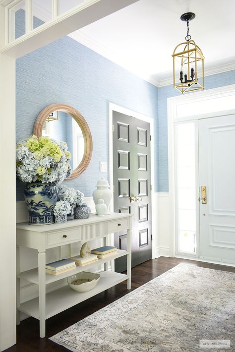 A bright and airy entryway with blue grasscloth is decorated for summer with gorgeous blue and white jars and vases arranged with gorgeous light blue and green hydrangeas. Light Blue Foyer, Hydrangea Blue Paint, Airy Entryway, Coastal Foyer, Blue Grasscloth, Blue And White Ginger Jars, Wallpapered Entryway, Spring Kitchen Decor, Entryway Inspiration