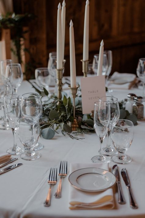 Simple, stunning table setting, white tablecloths, napkins, table number cards, beautiful greens and candles as centerpieces, Wedding, The Barns at Wesleyan Hills Candlestick Tablescape, Wedding Table Candlesticks, Candlestick Centerpiece, England Winter, Rustic Elegant Wedding, Candle Wedding Centerpieces, Circle Table, Event Centerpiece, Simple Elegant Wedding