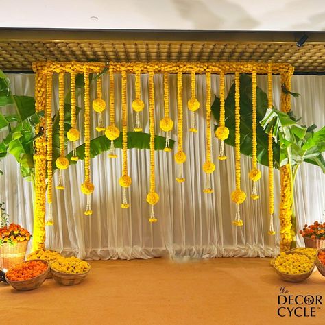 Simple and elegant South Indian Haldi Decor with genda phool and banana leaves. Backdrop Decoration. #southindian#haldi#mehendi#wedding#indianwedding#yellow#orange#genda#haldidecor#thedecorcycle Haldi Decoration Ideas At Home Terrace, Yellow Backdrop Decorations, Simple Haldi Decoration At Home Terrace, South Indian Haldi Decor, Rice Ceremony Decoration Indian, Pasupu Decor, South Indian Haldi, Haldi Background Decoration, Indian Haldi Decor