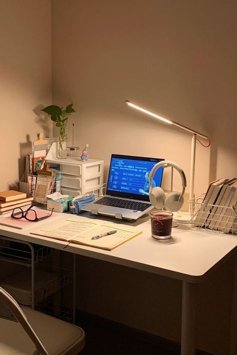 A minimalist study desk setup with a laptop, open notebook, reading lamp, headphones, and a calming candle. The desk also includes books, a plant, and organizational drawers, creating a warm and inviting space perfect for studying or working Simple Work Setup, Laptop Only Desk Setup, Small Tech Office Design, Notebook Desk Setup, Minimalist Laptop Setup, Laptop Desk Setup Small Spaces, Small Cozy Desk Setup, Desk Risers Ideas, Uni Desk Setup