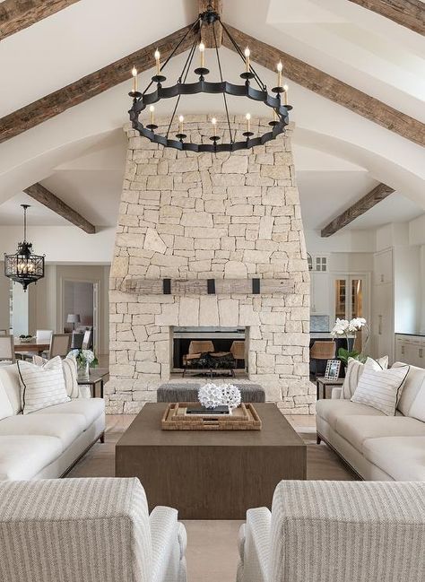 Brown oak block coffee table centered between ivory roll arm sofas in a cottage living room boasting vaulted ceilings, an iron candelabra chandelier, and a beige stone fireplace. Cathedral Ceiling Living Room, Block Coffee Table, Cottage Living Room, Cottage Living Rooms, Fireplace Remodel, Home Fireplace, Fireplace Makeover, Cottage Living, Living Room With Fireplace