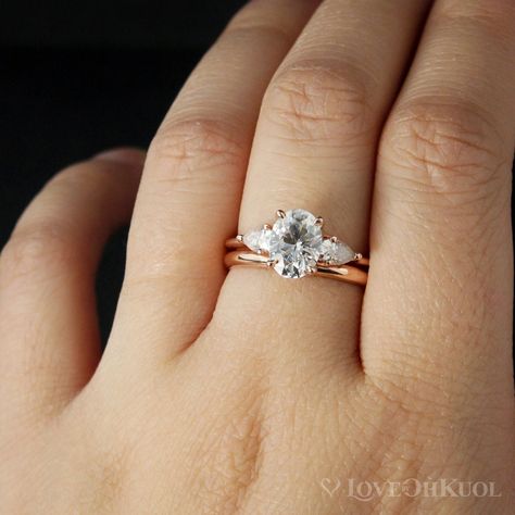 Here is a gorgeous 3 stone engagement ring with classic clean lines. The center stone features a stunning oval brilliant -cut Forever One Colorless D/E/F grade Moissanite, accented with two pear-cut Forever One Colorless moissanites on each side. The band is half round and is 1.5mm wide. The raised shoulders allows this ring to stack easily with all our wedding bands. This ring is also available with a round center stone too.  Paired together with our Comfort Fit Wedding Band. The wedding band h Three Stone Engagement Rings Oval, Wedding Ring Sets Simple, Rose Gold Wedding Ring Sets, Gold Band Wedding Ring, 14k Rose Gold Wedding Ring, Trilogy Engagement Ring, Comfort Fit Wedding Band, Moissanite Engagement Ring Oval, 3 Stone Engagement Rings