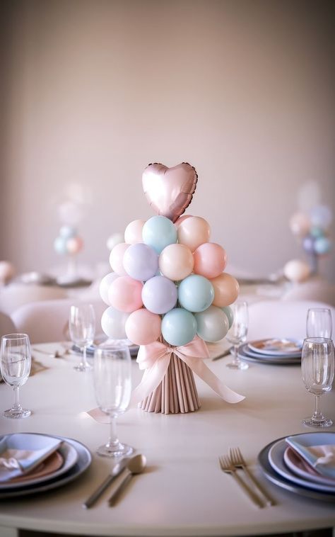 A pastel-themed baby shower centerpiece with balloons in shades of pink, blue, and white, arranged like a topiary. A heart-shaped balloon tops the display. The table is set elegantly with plates, cutlery, and glasses for a soft ambiance, offering delightful centerpiece ideas. Unique Centerpiece Ideas, Baby Shower Centerpiece Ideas, Balloon Baby Shower Centerpieces, Balloon Table Centerpieces, Storybook Theme, Party Event Ideas, Pop Baby Showers, Small Balloons, Unique Themes