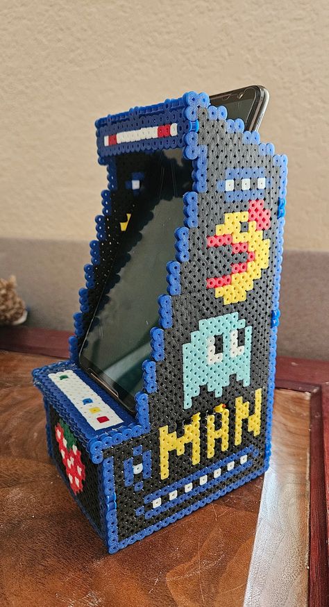 This Pac-Man arcade cabinet perler bead pdf cellphone holder is the perfect combination of retro gaming and practicality.  Key features: - Handmade with perler beads - PDF pattern for DIY crafting - Fits most cellphone models - Fun and unique Pac-Man arcade cabinet design Crafted with colorful perler beads, this Pac-Man inspired cellphone holder is a nostalgic throwback to classic arcade gaming. The included PDF pattern allows for easy DIY crafting, so you can create your own personalized version of this fun accessory. Designed to fit most cellphone models, this holder is both functional and stylish. Its unique design features a mini Pac-Man arcade cabinet complete with joystick and buttons. Overall, this quirky little accessory makes a great gift for any retro gaming enthusiast or anyone Perler Bead Display, Perler Bead Headband, Perler Bead Games, Perler Bead Computer, Perler Bead Glasses Holder, Perler Bead Phone, Game Perler Beads, Perler Bead Patterns Video Games, Perler Beads Hello Kitty