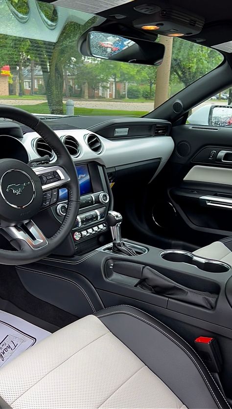 Interior of a 2022 Ford Mustang GT Coupe Premium with light and dark dual-toned interior seating parked at Bill Brown Ford in Livonia, Michigan. Surrounding the vehicle is green grass and a tree, which can be seen through the front windshield. White Ford Mustang Gt, Mustang Interior Aesthetic, 2022 Mustang Gt, Car Interior Wallpaper, Ford Mustang Gt Interior, Mustang Gt Interior, Mustang Steering Wheel, Ford Mustang History, 2022 Mustang