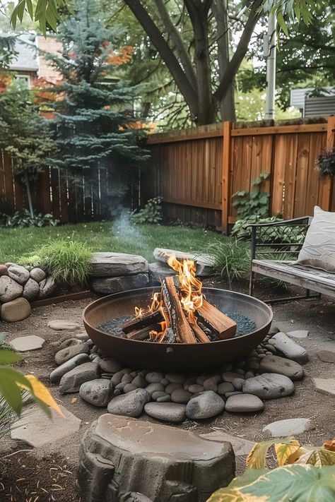 A cozy backyard with a fire pit surrounded by rocks, a wooden fence, and lush green trees and plants, perfect for relaxing outdoors.