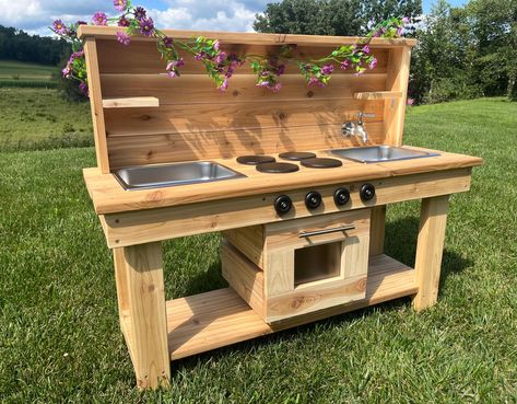 Liven up your outside playtime with this stunning centered mud kitchen with oven! Handmade in the USA from cedar wood, this durable and charming play kitchen is sure to provide hours of outdoor fun and sensory play. These educational toys are the perfect addition to backyards, daycare centers and schools. This double sink mud kitchen includes two stainless steel bins, shelves and pegs to store toys, an oven and options to include stovetops, knobs, faucets and drains.    Materials & Finish: Our m Play Kitchen Outdoor, Kids Outdoor Kitchen Diy, Kids Kitchen Set, Mud Table For Kids, Kids Outdoor Kitchen, Pallet Mud Kitchen, Outdoor Mud Kitchen, Diy Mud Kitchen Outdoor Play, Pallet Mud Kitchen Diy Plans