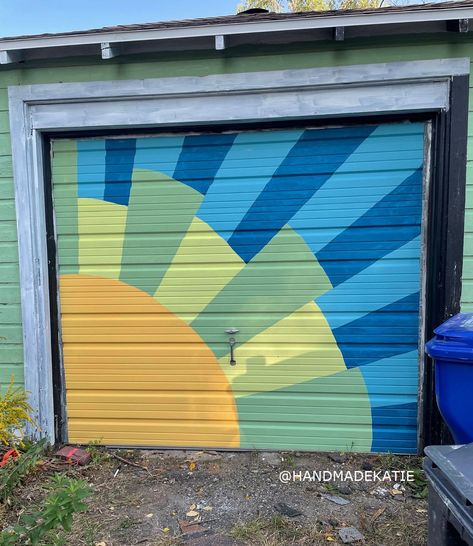 A sunburst mural is on a garage door. Mural Garage Door, Garage Door Mural Ideas, Barn Murals Ideas, Sunburst Mural, Mural On Shed, Garage Mural Ideas, Simple Mural Ideas, Backyard Mural Ideas, Pretty Fence