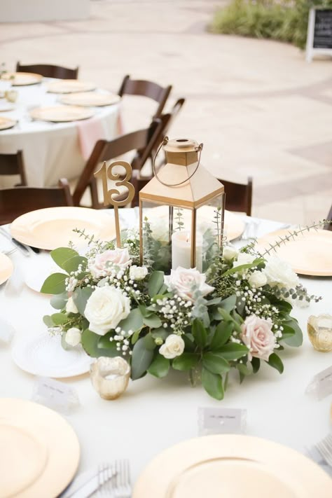 Rustic Nautical Outdoor Wedding Reception Round Table Decor with Gold Hurricane Lantern and Low White Rose with Greenery Centerpiece, Gold Chargers and Tea Candles, Light Blue Tablecloth and Pink Linens, and Brown Wood Folding Chairs Blue Table Decorations, Summer Table Decorations, Lantern Centerpiece Wedding, Round Table Decor, Greenery Centerpiece, Lantern Centerpieces, White Lanterns, Tafel Decor, Wedding Lanterns