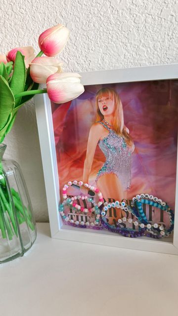 Sickbugg | Croc Charms, Accessories & Decor Inspo on Instagram: "The cutest way to display your Taylor Swift Eras Tour movie poster & friendship bracelets 🫶 @taylorswift Frames are currently half off @michaelsstores ✨ #erastourtaylorswift #erastourmovie #amc #taylorswift #swifties" Friendship Bracelets Display, Taylor Swift Bracelet Display, Eras Tour Accessories, Poster Friendship, Movie Poster Display, Music Bracelet, Bracelet Storage, Music Room Decor, Taylor Swift Tour Outfits