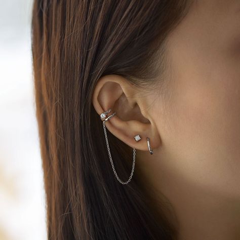 A unique conch ear cuff that features a chain and connected stud earring. Bendable for a snug fit. Sold as a single earring. Sterling Silver Cubic Zirconia, prong setting Hypoallergenic, lead and nickel free Inner diameter 9mm x Band Thickness 1.5mm Crystal 3mm Chain Length 2.75in Bendable for a snug fit #E515-Sx1 Unique Ear Cuffs, Minimalist Ear Piercings, Different Ear Piercings, Unique Ear Piercings, Ear Peircings, Ear Cuff Chain, Earring Cuff Chain, Types Of Ear Piercings, Cool Ear Piercings