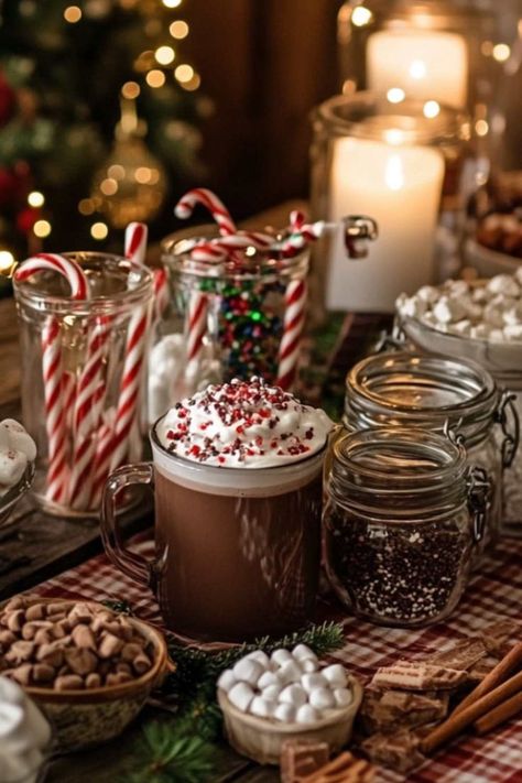 A festive hot chocolate bar featuring jars of candy canes, sprinkles, marshmallows, and a mug of hot cocoa topped with whipped cream and peppermint pieces. Lit candles and a Christmas tree add a cozy holiday ambiance in the background. Winter Date Night Ideas, Parisian Picnic, Indoor Picnic, Diy Hot Cocoa, Winter Date Night, Bar Setup, Holiday Hosting, Cozy Drinks, Holiday Dates