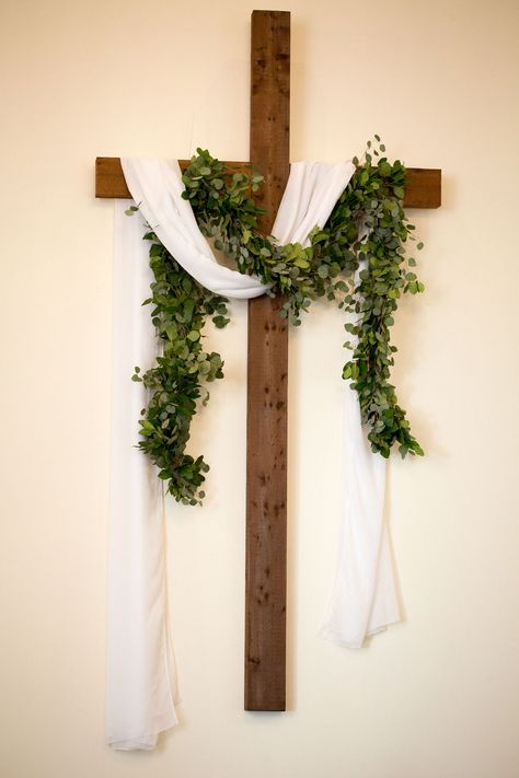 Wooden cross with white linen sash and thick greenery swag Easter Cross With Flowers, Wooden Cross Decor, Ordinary Time Church Decor, Easter Flower Arrangements For Church, Easter Church Decor, Cross Arrangements, Church Decorations Ideas, Ceremony Cross, Lent Decorations For Church