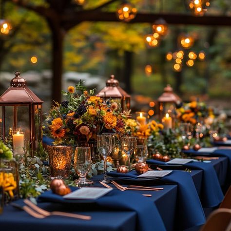 A bold wedding setting featuring navy blue bridesmaid gowns with copper jewelry, illuminated by copper lanterns and table settings, and vibrant autumnal flowers in shades of orange and yellow. Navy Blue And Sunset Orange Wedding, Dark Blue And Burnt Orange Wedding, Navy And Terracotta Wedding Table, Blue And Orange Wedding Centerpieces, Blue Wedding Theme Fall, Blue And Orange Wedding Table, Van Gogh Wedding Theme, Terracotta Navy Wedding, Fall Wedding Dark