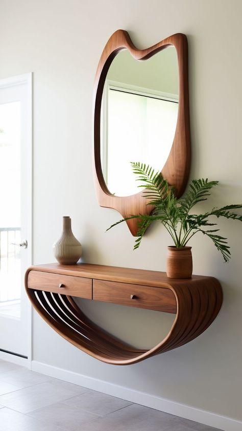 A wall-mounted console table and mirror set. The console table has an organic, curved design resembling a wave or a ribbon, with a flat surface on top for placing objects and an open shelf area underneath. It is made of wood with a rich, warm tone that complements the similarly styled wooden frame of the mirror above it. The mirror has an asymmetrical shape, wider at the top and tapering towards the bottom. By freepik Tiny Front Entry, Small Apartment Entrance, Small Entryway Decor Ideas, Apartment Entryway Decor, Small Open Concept, Mid Century Modern Entryway, Mid Century Entryway, Entryway Inspo, Wilfred Owen