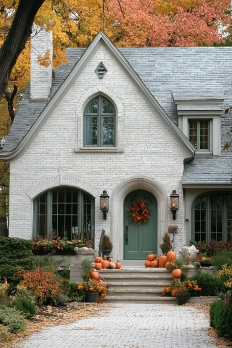 White brick house with pumpkins and green accents. The charm and quirks of 1920s houses, where elegance met the epitome of funky craftsmanship, all wrapped up with a touch of art deco flair. Victorian Cape Cod House, Small Brick Tudor Cottage, 1950s Brick House, White Brick Cottage Exterior, Tudor Cottage Exterior, Tudor Style Homes Exterior, Brick Tudor Exterior, Tan Brick House, Brick Cottage Exterior