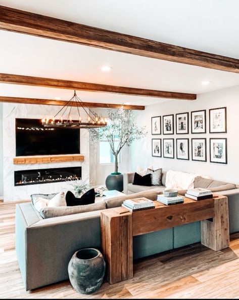 The warmth of the exposed ceiling beams in this bright living room adds just the right amount of contrast, making the space feel cozier. Use neutral earthy accent pieces like the black stone vases, solid wood console table, indoor tree, and wagon wheel chandelier for a modern finish. Beam Ceiling Ideas, Low Living Room, Rustic Wood Beams, Natural Wood Console Table, Exposed Wood Ceilings, Exposed Beams Ceiling, Beams Living Room, Beam Ceiling, Filler Ideas