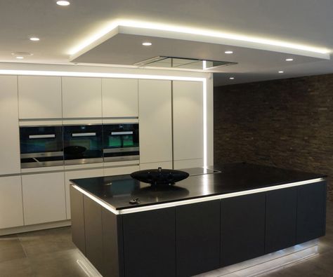 A monochromatic modern kitchen with lighting around the perimeter in addition to the small pot lights in the ceiling. To the right is a stacked stone wall. Kitchen Lighting Ideas For Low Ceilings, Contemporary Kitchen Island Lighting, Kitchen Ceiling Design, Blitz Design, Drop Ceiling Lighting, David James, Kitchen Ceiling Lights, Kitchen Ceiling, Bright Kitchens