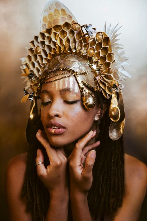 Beautiful woman with caramel skin and dreads wears a feminine, gold honey comb structured crown with gold drips of honey and fluffy white flowers.  She is looking down softly with hands gracefully resting under her chin on a mottled gold backdrop, from the shoulders up. Honey Costume, Gold Headdress, Queen Bee Costume, Bee Makeup, Theme Carnaval, Crown Headpiece, Bee Costume, Gold Costume, Bee Dress