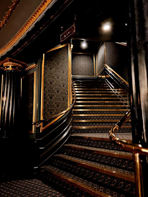 Dark gold grand curving staircase School Staircase Aesthetic, Dark Theatre Aesthetic, Dark Glam Aesthetic, Dark Gold Aesthetic, Dark Aesthetic Room, Dark Staircase, Theatre Architecture, Dark Mansion, 1920s Aesthetic