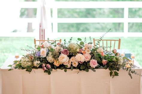 Sweetheart table arrangement by Sebesta Design featuring white cloud garden roses, white majolical spray roses, silver mikado spray roses, sweet escimo roses, lavender delphiunium, amnesia roses and local pee gee hydrangea framed by silver dollar, baby blue and seeded eucalyptus. Registrar Table Flowers, Sweetheart Table Arrangement, Communion Table Decorations, Cloud Garden, Pee Gee Hydrangea, Top Table Flowers, Amnesia Rose, Lavender Wedding Theme, Ski Wedding