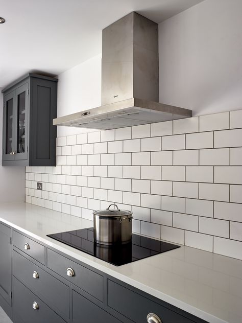 The white metro tiles create nice contrast with the Shaker kitchen cupboards painted in a dark grey colour, Little Greene 'Scree'. The worktops are Caesarstone 'Snow' in a polished finish and a 30mm thickness whilst the induction hob is T58FD20X0 from Neff. Also the freestanding stainless steel extractor is by Neff. The cup handles are from the Cotswold range by Armac Martin. Kitchen Tiles Grey Kitchen, Dark Grey Kitchen White Worktop, Metro Tiles Kitchen White, Grey Kitchen White Tiles, Grey Kitchen Tiles Wall, White Worktop Kitchen, Kitchen Metro Tiles, White Tiles Kitchen, White Kitchen Decor Ideas