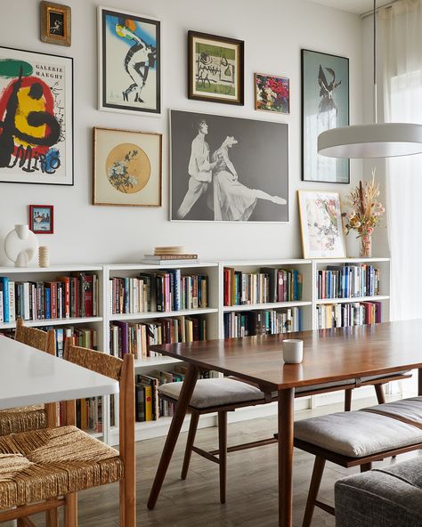 A curated gallery wall and lots of books give a lot of personality to this dining room, while the dining benches keep the space light and airy Library Dining Room Combo Modern, Apartment Dining Room Office, Narrow Dining Room Storage, Library Dining Room Combo Cozy, Dining Room With Bookshelf, Book Shelves In Dining Room, Dining Room With Library Wall, Dining Room Bookshelf Decor, Dining Room With Bookcases