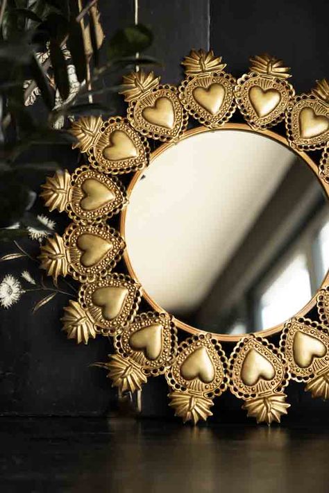 The Gold Milagro Heart Mirror takes our love of the ex-voto sacred heart symbol to a new level. Bold and beautiful, the gold frame mirror features detailed Milagro hearts joined together to create a round mirror unlike any other. A well-placed wall mirror can help reflect light around the room and brighten the darker corners of your home. As a result, we love how the glamorous gold finish of the decorative heart mirror pops against dark black or midnight walls. The perfect gift for a friend or l Sacred Heart Decor, Gold Hallway, Gold Frame Mirror, Milagro Heart, Round Gold Mirror, Catholic Decor, Gold Framed Mirror, Heart Mirror, Heart Decor