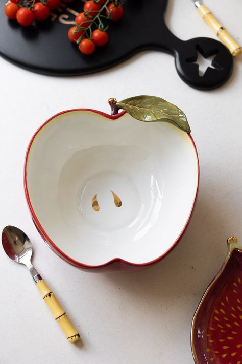 If you’re a fan of Italiana ceramic kitchen chic, you’ll love this beautiful apple-shaped serving bowl. It's a deep, roomy piece, and is exquisitely crafted, painted in a glorious deep red and apple white (of course). Particular care has been taken over the stem and leaf detailing, which are picked out in verdant green and glossy gold for an extra splash of sass. The golden pips at the bottom of the bowl are a lovely touch, too. Whether you indulge in a little family time, and use this for indul Fruit Ceramic Bowls, Ceramics Bowl Ideas, Apple Pottery, Food Ceramics, Apple Ceramic, Beautiful Kitchenware, Ceramic Apple, Verdant Green, Unique Plates