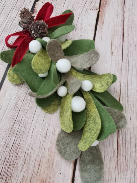 "This listing is for a One  delightful and whimsical sprig of mistletoe. It has been lovingly handcrafted from three shades of green wool blend felt which we have bonded together to give a sturdy, succulent look to the leaves. I add 100% wool ball \"berries\" and burgundy  red velvet ribbon. Hang it up and watch it delight all who pass under it. A wonderful gift! Hang it around the neck of a bottle of wine for a unique thank you gift for a host or hostess this holiday season. Felt flowers make a Felt Mistletoe, Spider Web Wreath, Acorn Garland, Mistletoe Christmas, Holiday Crafts Diy, Eco Friendly Decor, Decor Thanksgiving, Crochet Etsy, Felt Garland