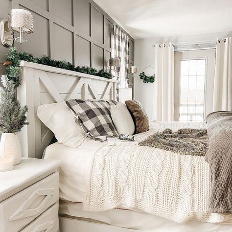 A farmhouse-style white wood headboard styled with pine garland is fitted with white and gray bedding. The bed stands in front of a gray board and batten accent wall next to a white nightstand. Bed Comforter Sets Farmhouse, Cozy Farmhouse Bedroom, Cream Bedroom, Rustic Farmhouse Bedroom, Farmhouse Bedroom Ideas, Modern Farmhouse Bedroom, Farmhouse Master, Country Bedroom, Farmhouse Bedroom Decor