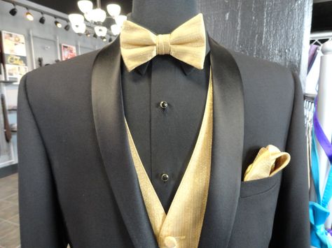 Be ready to steal any Belle away from the ball with this Black David Tutera tuxedo with our metallic gold bowtie, vest and pocket square combination. Tuxedo With Gold Accents, Black Tux Gold Vest And Tie, Champagne And Black Suits For Men, Gold Tie Black Suit, Black White And Gold Mens Suit, Black And Gold Wedding Tuxedo, Black And Gold Tuxedo Men, Gold Suits For Men Wedding Ideas, Black Tux Gold Tie