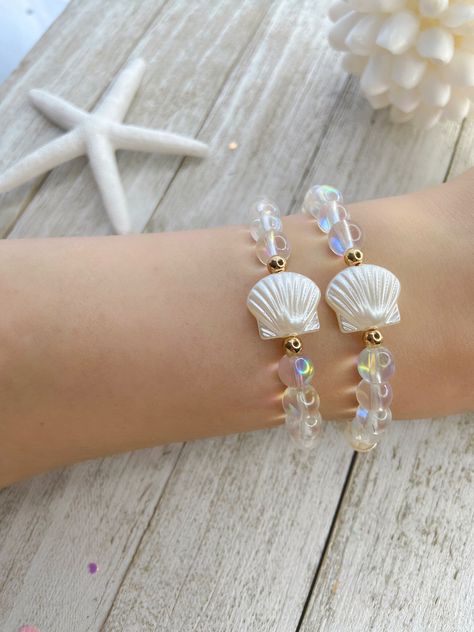 ⭐️⭐️ IRIDESCENT GLASS BEAD CLAM BRACELET ⭐️⭐️ Add mermaid vibes to your day with this iridescent clam bracelet! The listing is for one bracelet, images showing more than one are an example of how they would look stacked with other bracelets. Please choose your size from the drop-down menu. If you do not see your size there, send me a message with your size and I will be happy to make it for you. ♥ ITEM DETAILS ♥ 8mm Clear glass iridescent beads 4mm Gold plated beads 14mm Acrylic clam bead Sturdy stretchy elastic Your bracelet will come in a drawstring bag, ready to be gifted. If you are purchasing multiple bracelets and would like them packaged separately, please leave me note at checkout. All sales are final. If you have any questions, please feel free to message me. ♥ CARING TIPS ♥ Keep Beach Vibe Bracelet, Shell Bead Bracelet, Glass Beads Bracelet Ideas, Bracelet Images, Beads Craft Kids, Bracelets Rainbow, Mermaid Vibes, Multiple Bracelets, Mermaid Bracelet