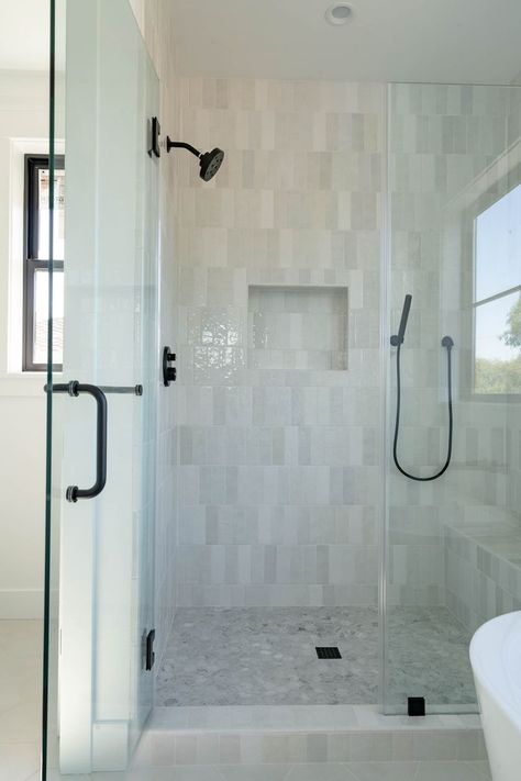 Primary Bathroom shower with Bedrosian's Cloe shower tile in a vertical offset pattern, Delta bathroom fixtures, black Anderesen 100 window, and large scale hexagon flooring. #thedendesingroup #interiordesign #shower #showerbench #handheld #siliconvalleyinteriordesign #redwoodcity #farmhouse #bathroom #primarybathroom #blackwindows #bedrosians #andersenwindows #bayareainteriordesign #luxuryrealestate #whitewalls #madeforliving Bathroom Fixtures Black, Vertical Shower Tile, Hexagon Flooring, Black Shower Fixtures, Large Shower Tile, Den Design, Master Bath Shower, New House Bathroom, White Bathroom Tiles