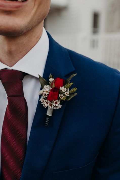 Get inspired by this red wedding boutonniere on a navy suit and burgundy tie. For more on this wedding visit our blog. Groom Navy Blue Suit Burgundy Tie, Red And Blue Boutonniere, Navy Suit Red Tie, Dark Blue And Red Wedding Theme, Navy Suit Burgundy Tie, Red And White Boutonniere, Navy And Red Wedding, Navy Red Wedding, Navy Winter Wedding