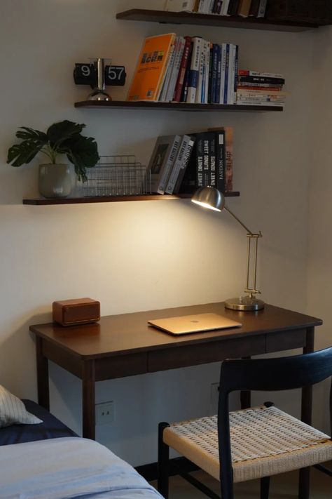 A minimalist dark wood desk with a modern table lamp, a laptop, and retro-style decor. Floating shelves hold books and plants, adding to the cozy and functional setup. This compact workspace is perfect for small spaces and a relaxed, focused environment. Writing Desk Bedroom, Minimal Desk Aesthetic, Retro Desk Setup, Working Desk In Bedroom, Small Desk Ideas Bedrooms, Study Desk Minimalist, Desk With Shelves Above, Setup Minimalista, Simple Desk Setup