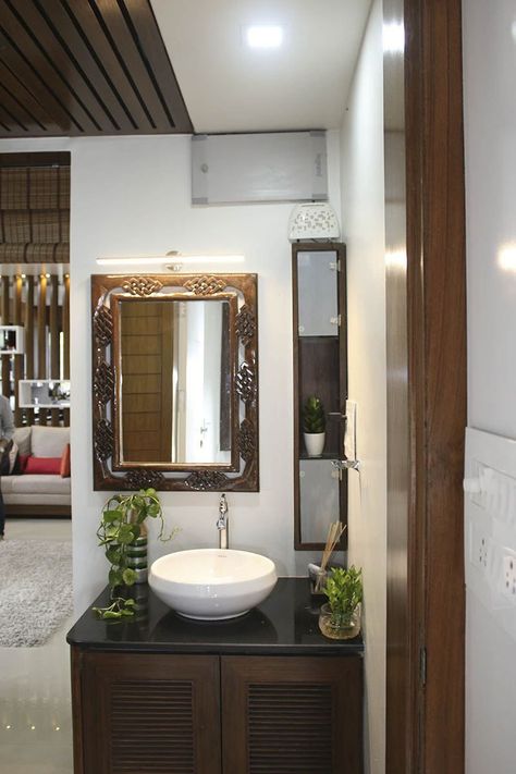 Common Basin Area incorporating Table Top Wash Basin on Black Granite Counter with Indoor Plants, Wooden Cabinet having Louvered Doors, Wall Mounted Rectangular Mirror with Wooden Frame highlighted with Wall ✨ Light and Vertical Wooden Cabinet with Glass Doors and Open Display Cabinet - GharPedia Table Top Sink Design, Granite Washbasin Counter, Basin With Cabinets, Basin Cabinet Design Modern, Pvc Farnichar, Granite Table Top Wash Basin Ideas, Wash Basin Cabinet For Living Room, Wash Basin Ideas In Living Room Indian, Table Top Basin Counter Design