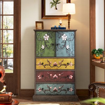 This boho-inspired accent cabinet features a hand-painted floral motif that adds a rustic touch to your living room, entryway, or bedroom. Crafted from engineered wood, it has a brown finish with green, pink, and yellow accents, complemented by black metal hardware. The cabinet includes three drawers with roller glides for smooth operation and removable knobs. Its bracket-style base reinforces the solid structure while keeping the cabinet away from moisture, ensuring your items stay dry. Additio Dining Room Essentials, Cabinet Wood, Accent Chest, Door Cabinet, Yellow Accents, Accent Cabinet, Fir Wood, Double Door, Paint Furniture