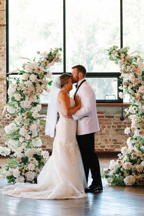 This wedding ceremony at the Biltwell Event Center included a symmetrical open arch finished with with and blush pink florals. The elegant floral wedding ceremony arch was a beautiful contrast against the industrial walls of the Biltwell Event Center. Save this photo to your wedding planning board as inspiration for your wedding ceremony arch. Floral Arch For Wedding Ceremony, All White Arch Wedding, Wedding Half Arch Flowers, Wedding Half Arch, Deconstructed Arch Wedding, Open Arch Wedding, Deconstructed Wedding Arch, White And Pink Wedding Arch, Partial Floral Arch Wedding