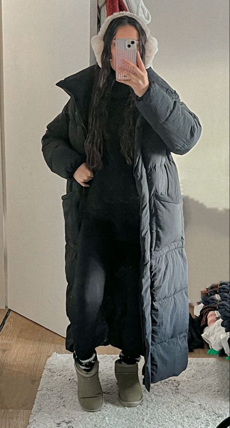 a mirror photo of a girl with mermaid wavy hair. She is wearing a black high neck jumper paired with black seamless leggings. to add an extra layer or warmth she is also wearing black fluffy socks with khaki ugg ultra minis and a long puffer padded black coat. to keep her even warmer she is wearing brown ear muffs Maxi Puffer Coat Outfit, Ear Muff Outfit, Padded Coat Outfit, Styling Black Leggings, Ear Muffs Outfit, Boots Black Outfit, Puffer Jacket Aesthetic, Mini Ugg Outfit, Earmuffs Outfit