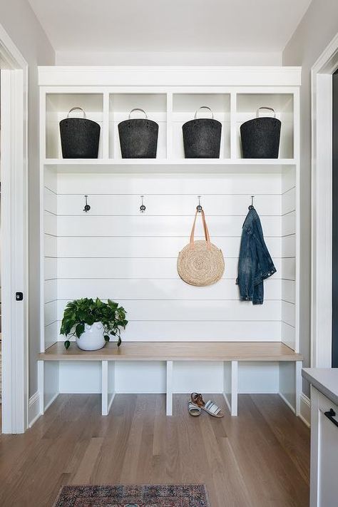 This welcoming mudroom features a light wooden bench fixed against a shiplap backsplash beneath coat hooks mounted under white cubbies holding black baskets. Entry Way Built In Bench With Storage, Shiplap Nook Wall, Kitchen Nook Mudroom, Built In Bench Open Underneath, Custom Entry Bench, Mudroom Seating Ideas, Open Bench Seating, White Oak Mudroom Bench, Entry Way Bench Built In